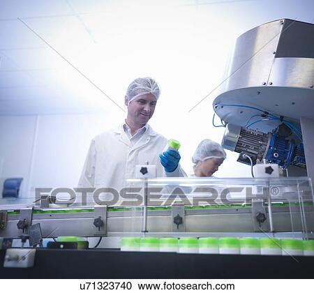 Stock Image - Workers inspecting products on production line in pharmaceutical factory. Fotosearch