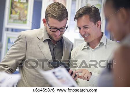 Stock Photograph - Young businessman looking at colleagues digital tablet. Fotosearch