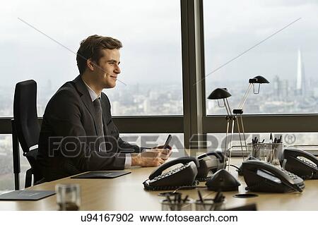Stock Image - Young businessman sitting at boardroom table. Fotosearch