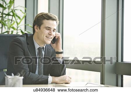 Young businessman talking on smartphone from office View Large Photo Image Stock Photo - Young businessman talking on smartphone from office. Fotosearch