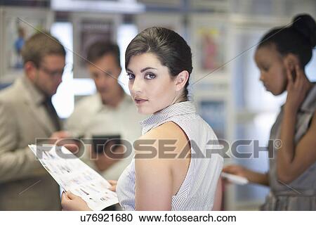 Stock Image - Young businesswoman looking over her shoulder in meeting. Fotosearch
