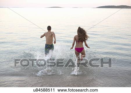 Stock Image - Young couple running into the sea together, Orebic, Croatia. Fotosearch