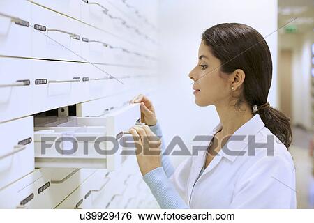 Stock Photograph - Young female pharmacist searching for medicine for prescription. Fotosearch