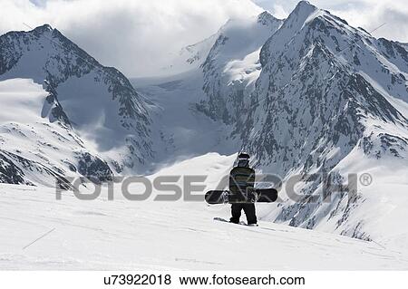 Stock Photo - Young male snowboarder walking up mountain, Obergurgl, Austria. Fotosearch