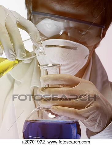 Stock Image - Young scientist carefully pouring liquid from flask. Fotosearch