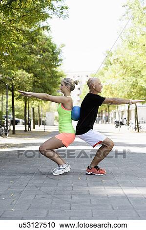 Stock Image - Young woman and trainer using exercise ball in park. Fotosearch