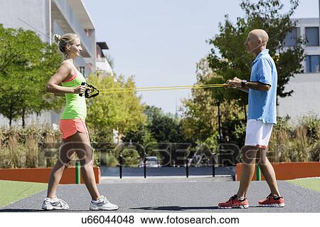 Stock Photo - Young woman and trainer using exercise ropes in park. Fotosearch