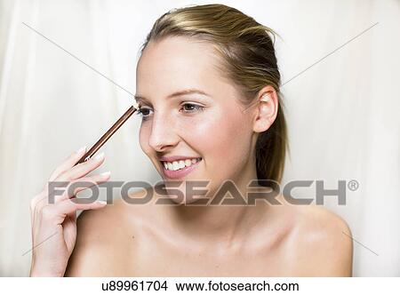 Picture - Young woman applying eye make-up. Fotosearch