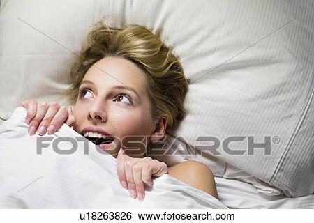 Stock Photograph - Young woman hiding under duvet. Fotosearch