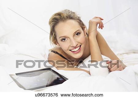 Young woman lying on bed with coffee and digital tablet View Large Photo Image Stock Photograph - Young woman lying on bed with coffee and digital tablet. Fotosearch