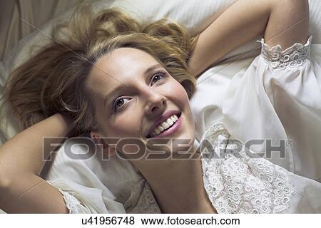 Young woman lying on bed with hands behind head View Large Photo Image Stock Photo - Young woman lying on bed with hands behind head. Fotosearch