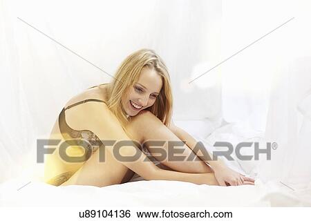Stock Photograph - Young woman sitting on bed wearing underwear. Fotosearch