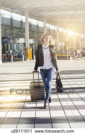 Young woman walking outside airport, pulling wheeled suitcase View Large Photo Image Stock Image - Young woman walking outside airport, pulling wheeled suitcase. Fotosearch