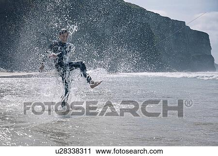 Stock Image - Boy wearing wetsuit, splashing in sea. Fotosearch