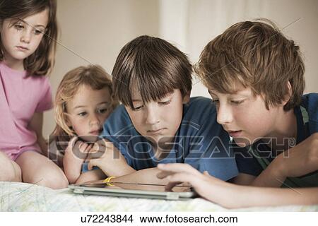 Brothers and sisters lying on bed looking at digital tablet View Large Photo Image Picture - Brothers and sisters lying on bed looking at digital tablet. Fotosearch