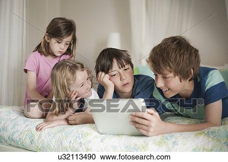 Brothers and sisters lying on bed playing with digital tablet View Large Photo Image Stock Image - Brothers and sisters lying on bed playing with digital tablet. Fotosearch