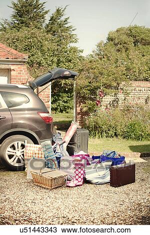 Stock Image - Car boot open with suitcases, baskets and bags prepared on drive. Fotosearch