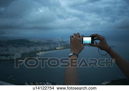 Picture - Close up of female hands photographing view of Rio De Janeiro at night, Brazil. Fotosearch