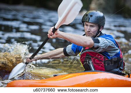 Stock Image - Close up of mid adult man kayaking on river rapids. Fotosearch