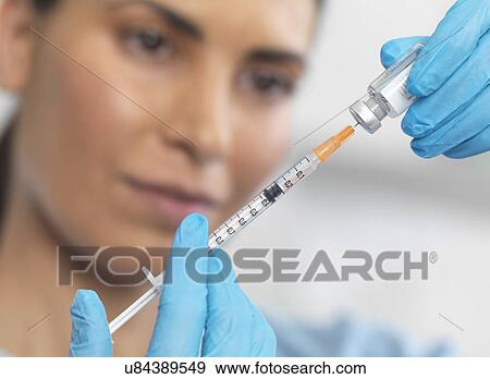 Stock Photo - Close up of nurse preparing a syringe for an injection. Fotosearch