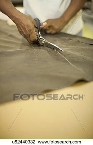 Stock Image - Close up of upholsterer cutting leather with scissors. Fotosearch