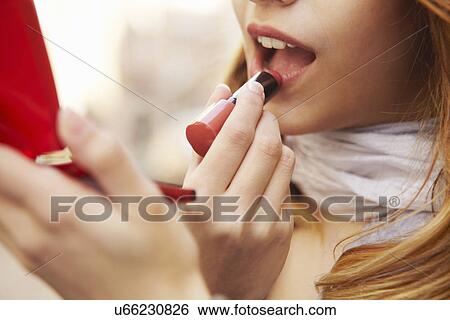 Stock Photograph - Close up of young woman putting on lipstick. Fotosearch