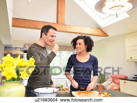 Picture - Couple in kitchen tasting and slicing peppers. Fotosearch