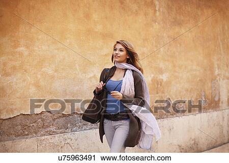 Stock Image - Elegant young woman strolling down street. Fotosearch