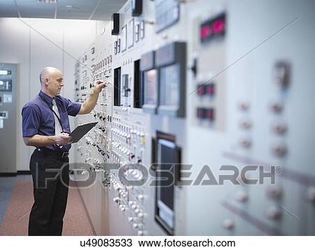 Stock Image - Engineer inspecting nuclear power station control room simulator. Fotosearch