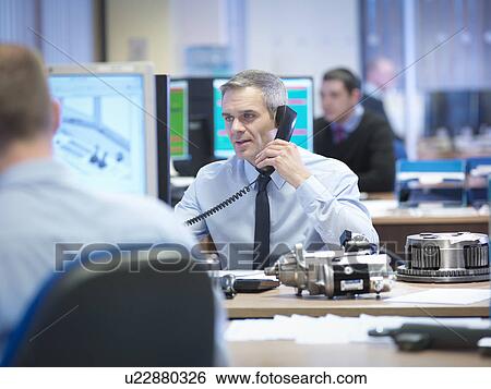 Stock Photograph - Engineer using telephone at desk in office. Fotosearch