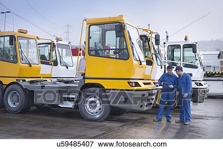 Stock Photo - Engineers inspecting parked trucks at truck repair factory. Fotosearch
