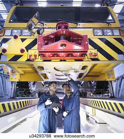 Stock Photo - Engineers inspecting underneath truck in repair factory. Fotosearch
