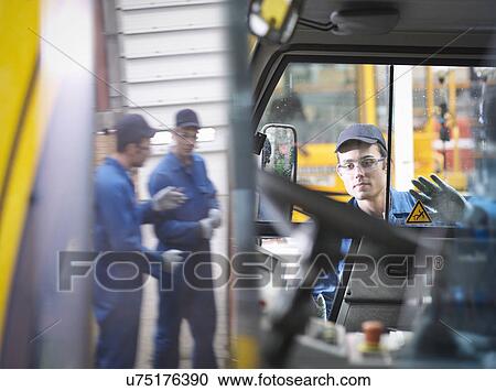 Stock Image - Engineers reflected in mirror in truck repair factory. Fotosearch