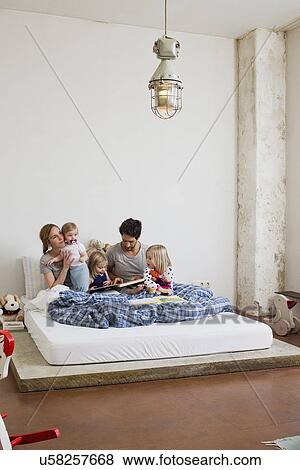 Family with three daughters reading books in bed View Large Photo Image Stock Photo - Family with three daughters reading books in bed. Fotosearch