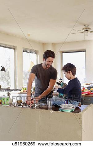 Stock Photo - Father and young son clearing up in kitchen. Fotosearch