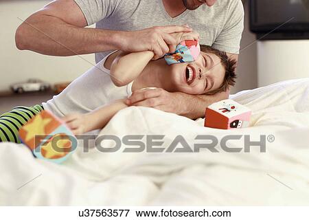 Stock Photo - Father and young son playing with building blocks on bed. Fotosearch