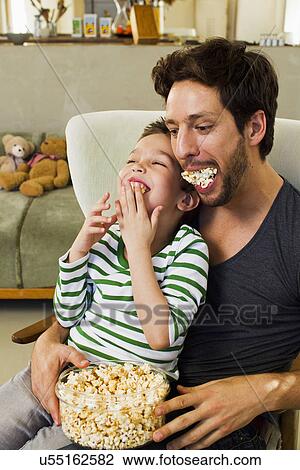 Stock Image - Father and young son with mouthfuls of popcorn. Fotosearch
