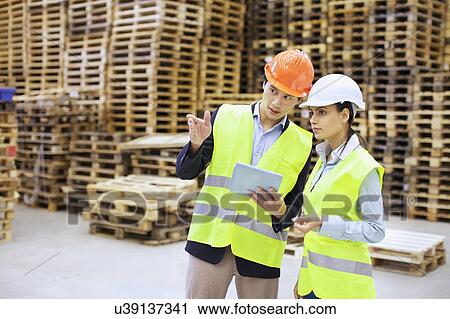 Stock Image - Male and female managers using digital tablet in distribution warehouse. Fotosearch