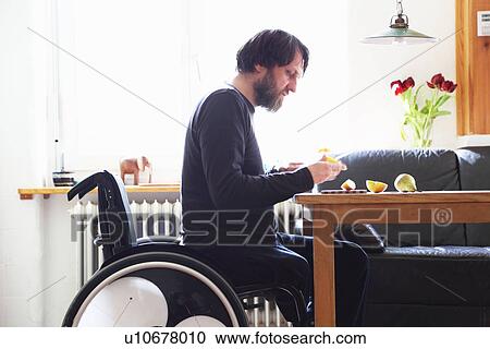 Stock Image - Man in wheelchair cutting fruit. Fotosearch