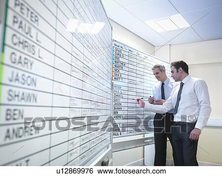 Managers writing notes on board in office View Large Photo Image Stock Photograph - Managers writing notes on board in office. Fotosearch