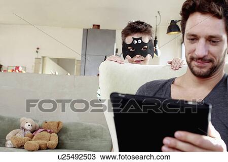 Masked son distracting father from digital tablet View Large Photo Image Stock Image - Masked son distracting father from digital tablet. Fotosearch