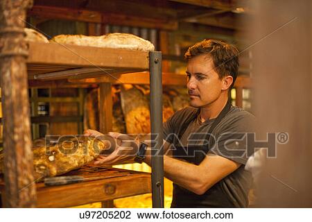 Stock Image - Mature man placing fresh bread on shelf. Fotosearch