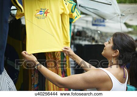 Picture - Mature woman looking at brazilian football shirt on market stall, Ipanema, Rio De Janeiro, Brazil. Fotosearch