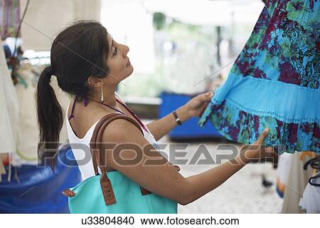 Stock Image - Mature woman looking at skirt on market stall, Ipanema, Rio De Janeiro, Brazil. Fotosearch