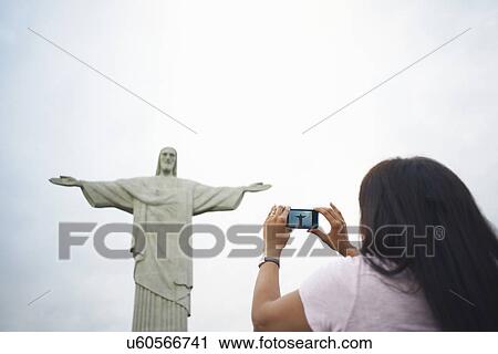 Stock Image - Mature woman photographing Christ the Redeemer, Rio De Janeiro, Brazil. Fotosearch