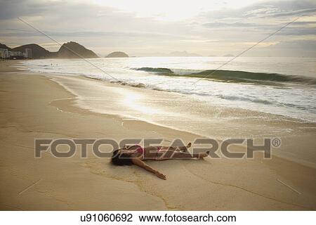 Stock Image - Mature woman sunbathing on Copacabana beach at sunset, Rio De Janeiro, Brazil. Fotosearch