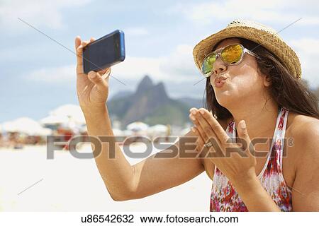 Stock Image - Mature woman taking a self portrait, Ipanema beach, Rio De Janeiro, Brazil. Fotosearch