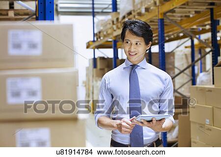 Mid adult male manager using digital tablet in distribution warehouse View Large Photo Image Picture - Mid adult male manager using digital tablet in distribution warehouse. Fotosearch