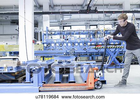 Mid adult male moving products on pallet jack in engineering plant View Large Photo Image Picture - Mid adult male moving products on pallet jack in engineering plant. Fotosearch