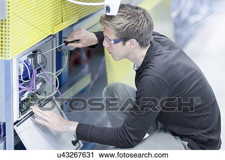 Stock Image - Mid adult male technician maintaining equipment in engineering plant. Fotosearch